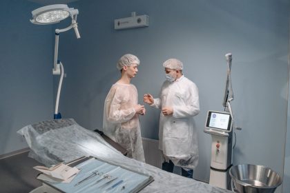Médico conversa com paciente em uma clínica, com equipamentos cirúrgicos ao fundo.