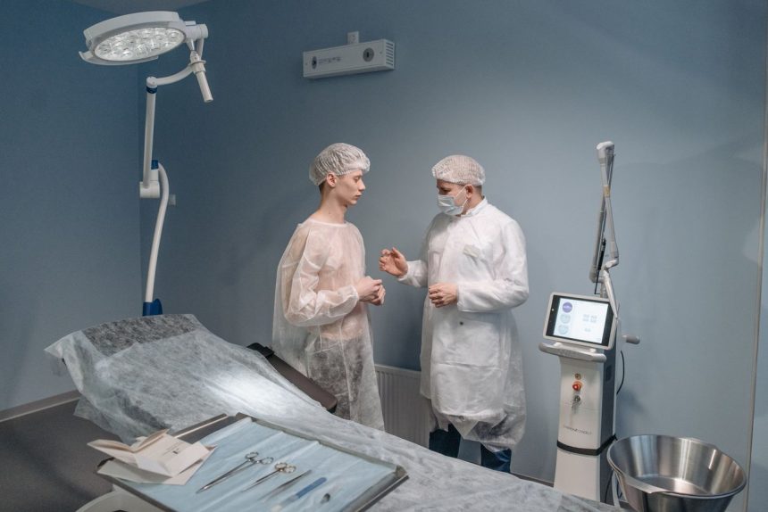 Médico conversa com paciente em uma clínica, com equipamentos cirúrgicos ao fundo.